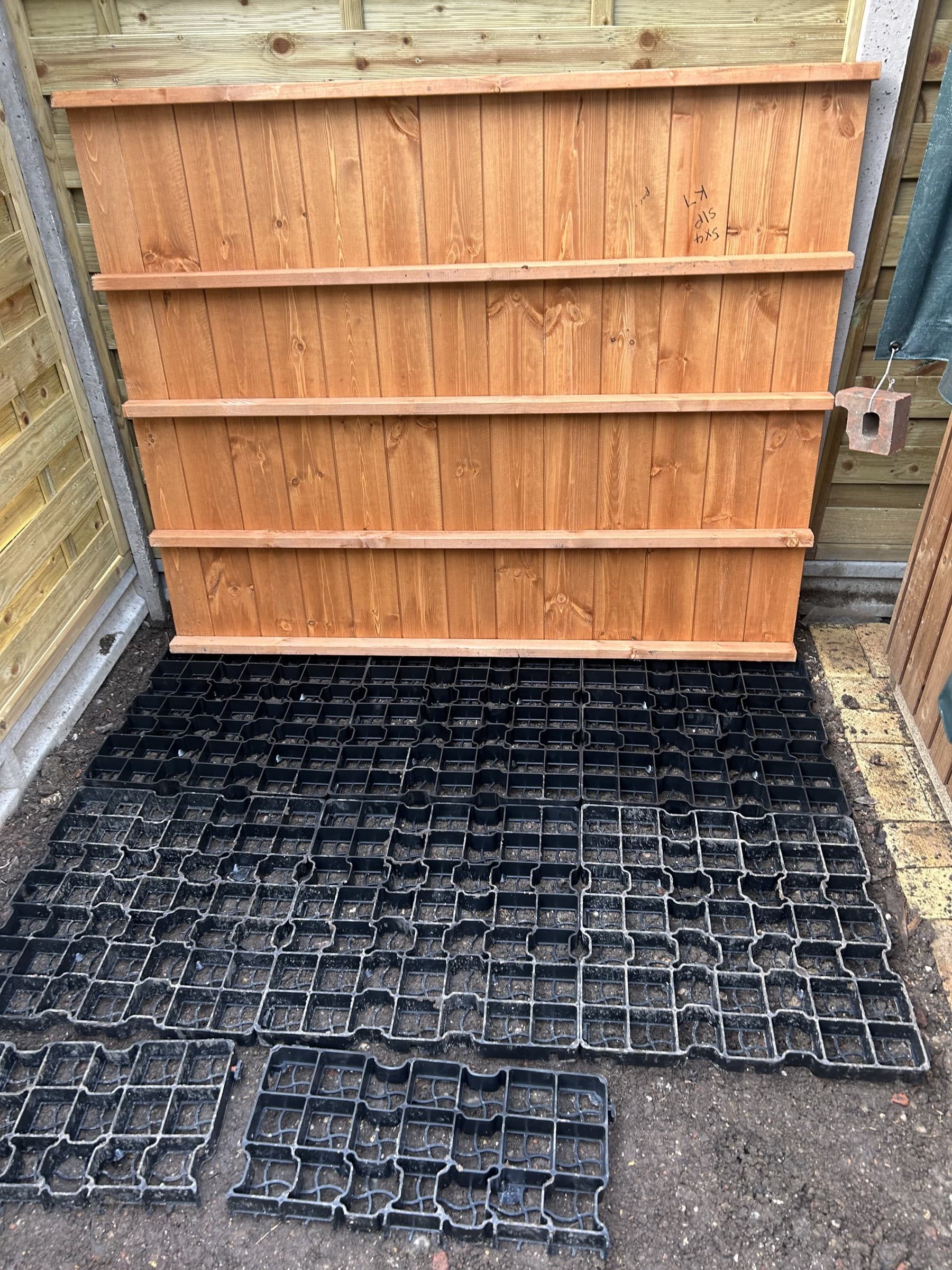 Fence panels and permeable paving grid base prepared in a garden before shed assembly