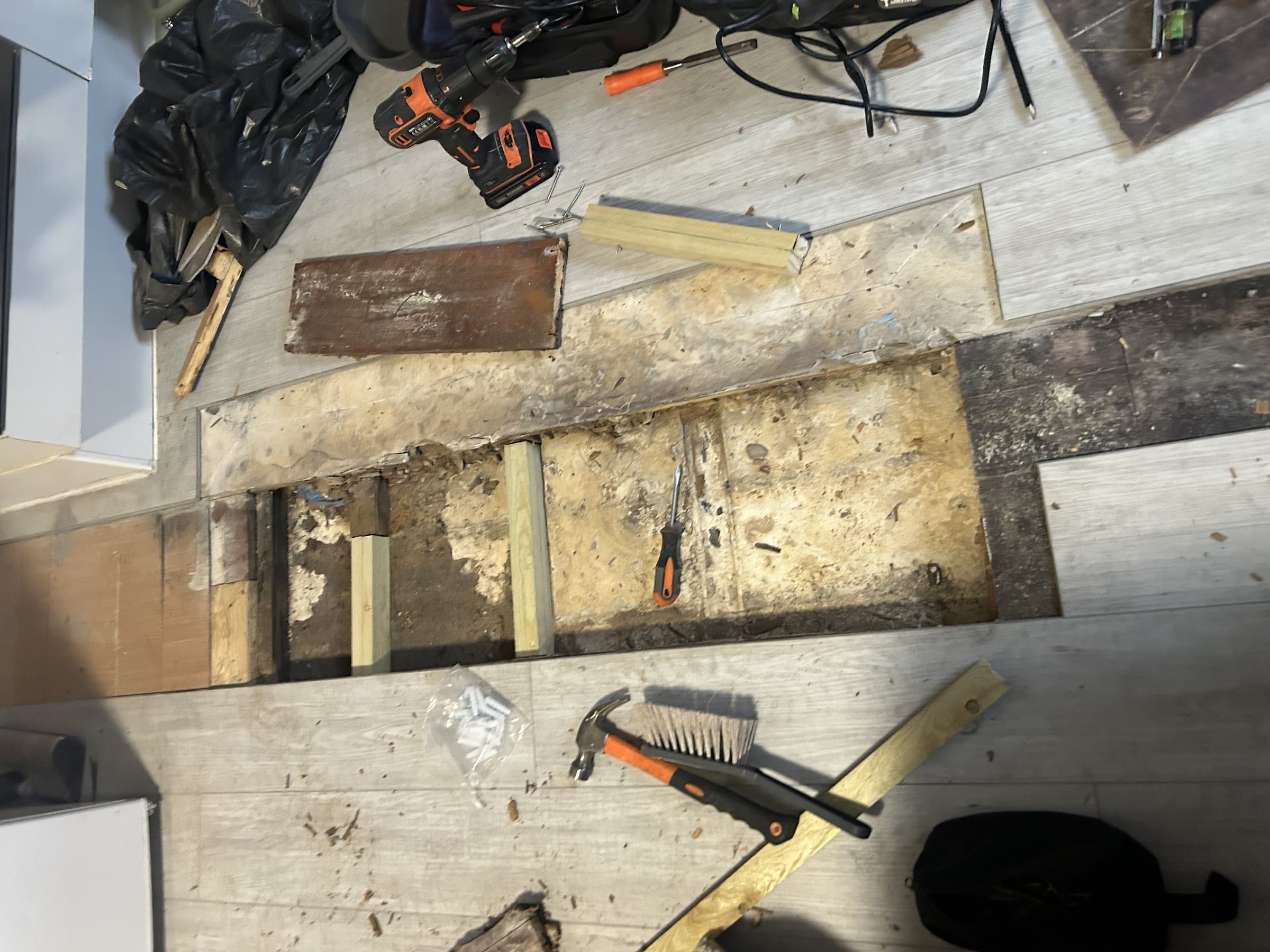 Damaged laminate flooring lifted to expose the subfloor, with repair tools laid out