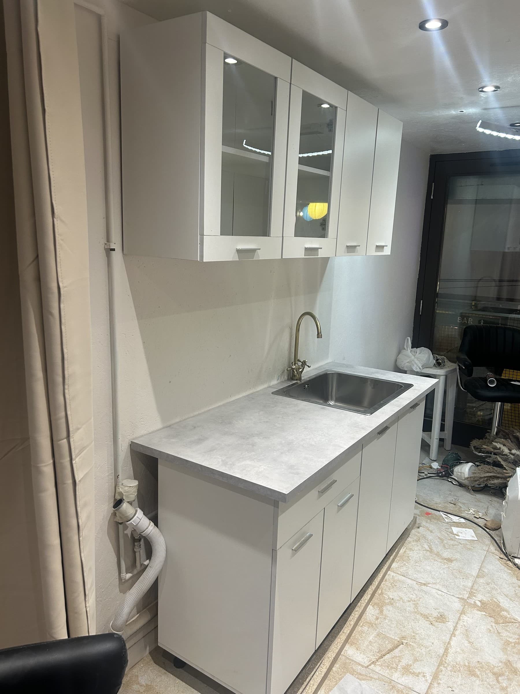 Finished small fitted kitchen with white cabinets and an inset stainless steel sink and mixer tap