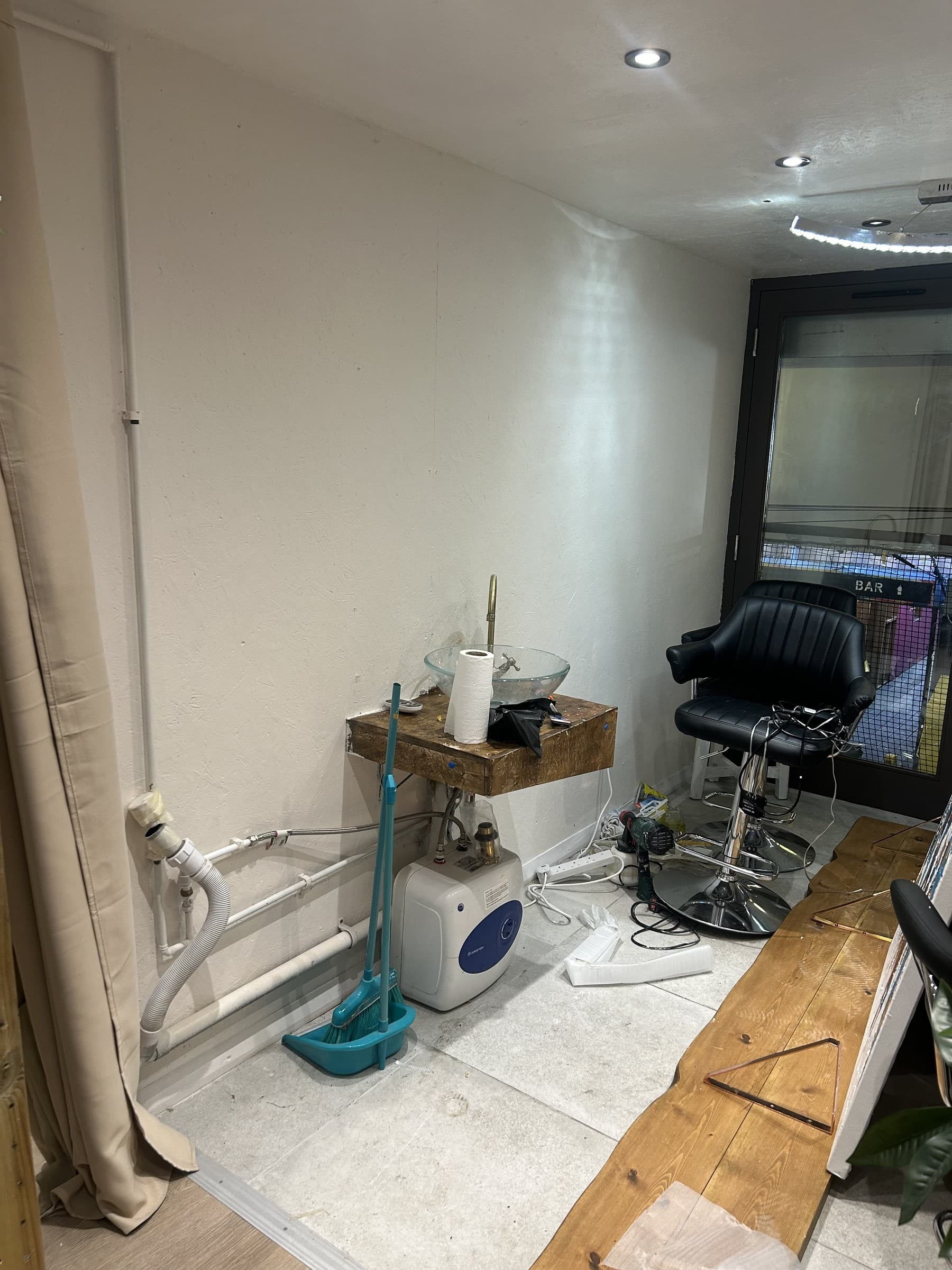Unfinished small utility room with a basin and pipework loosely connected on a temporary stand, before a small kitchen unit is fitted