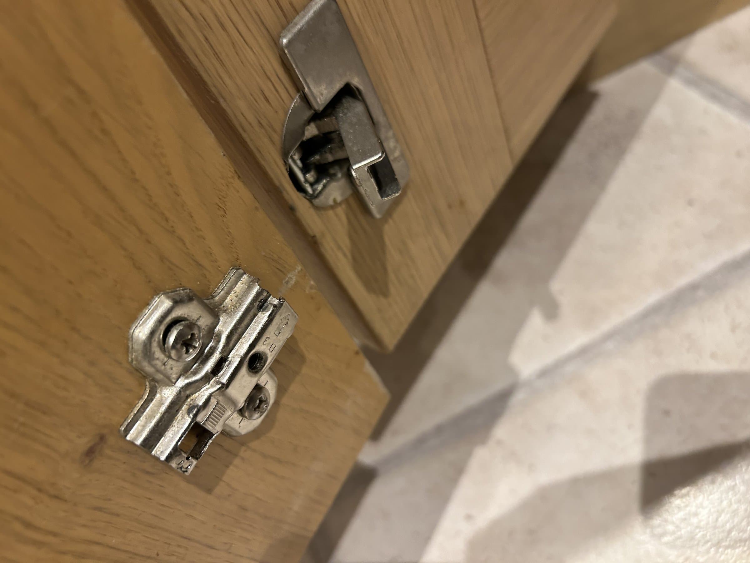 Loose cabinet door hinge and detached mounting plate before replacement