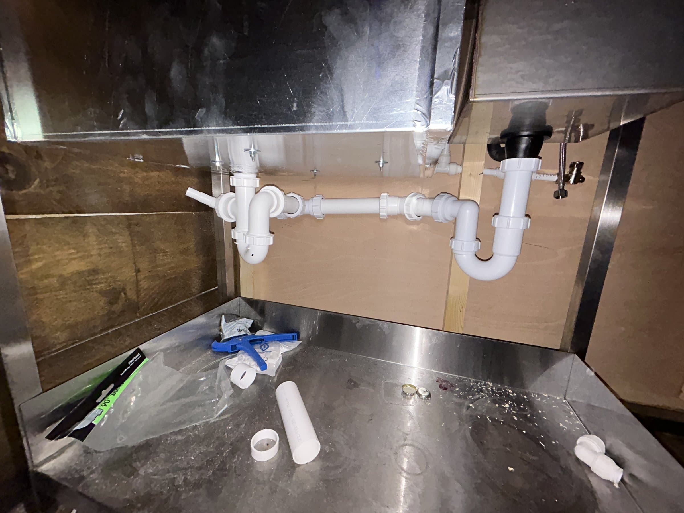 Waste pipes and traps connected under a stainless steel double kitchen sink