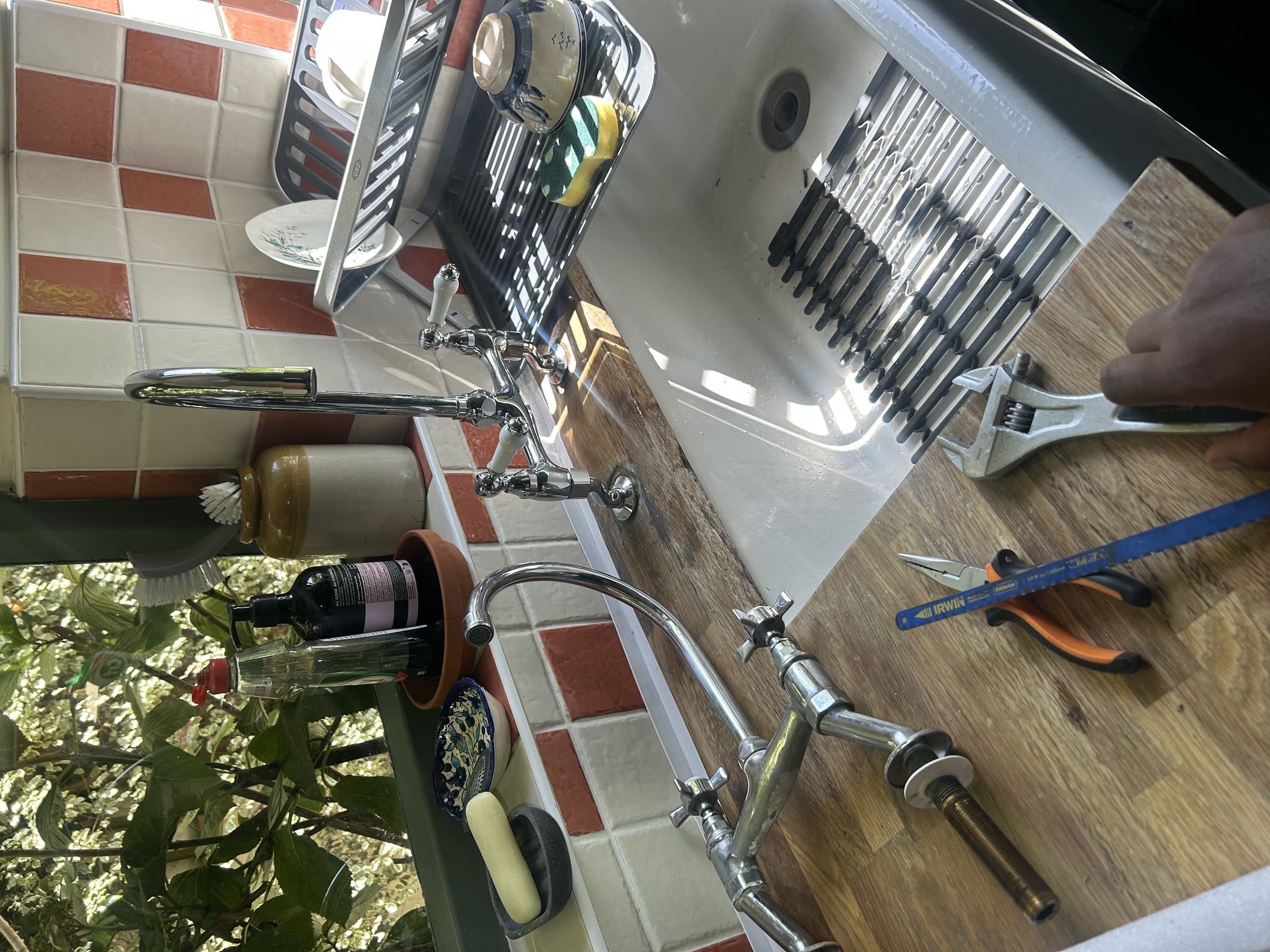 Traditional cross-head kitchen mixer tap installed on a Belfast sink, being adjusted with a wrench