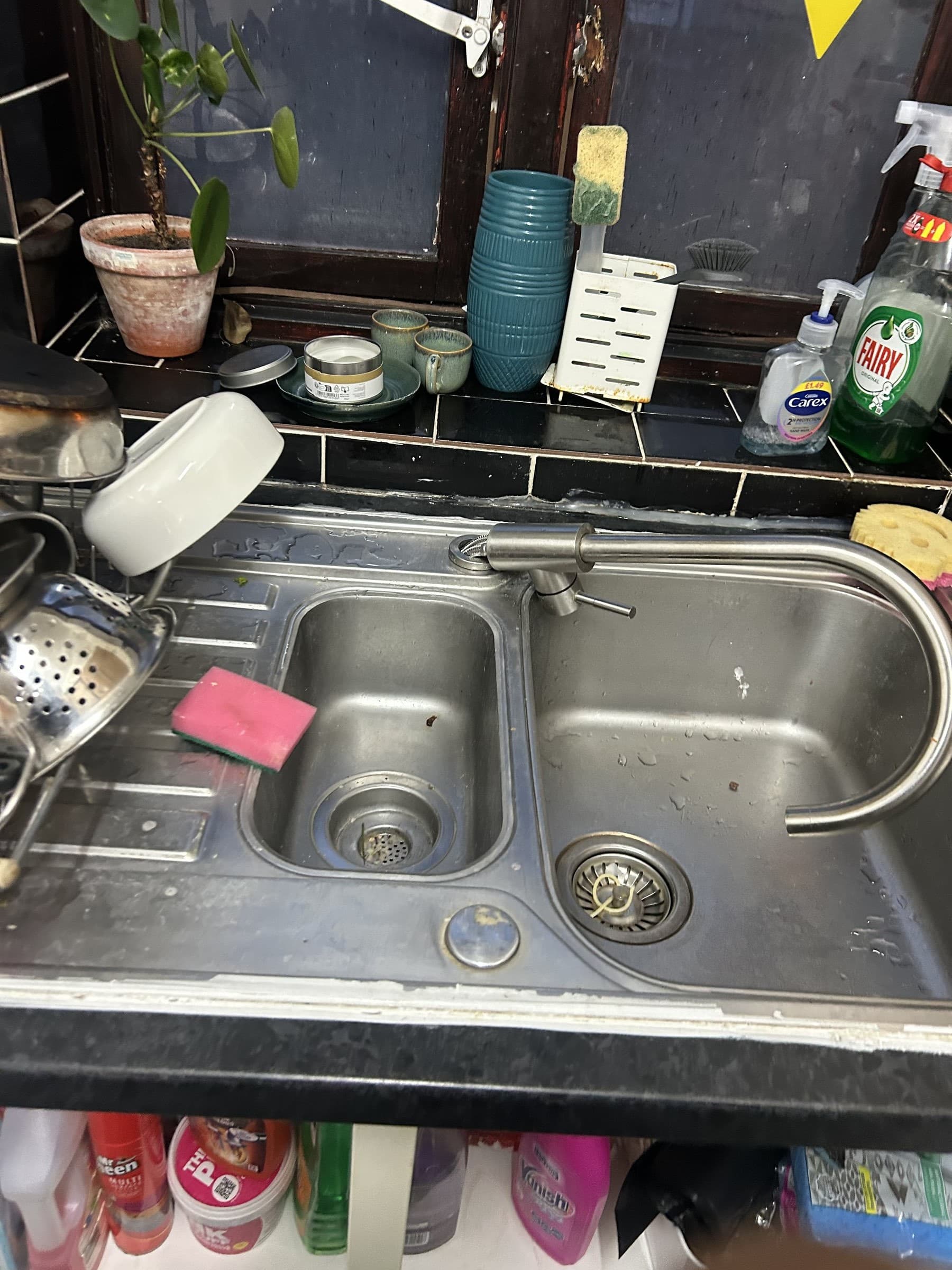 Old chrome gooseneck mixer tap on a stainless steel kitchen sink before replacement