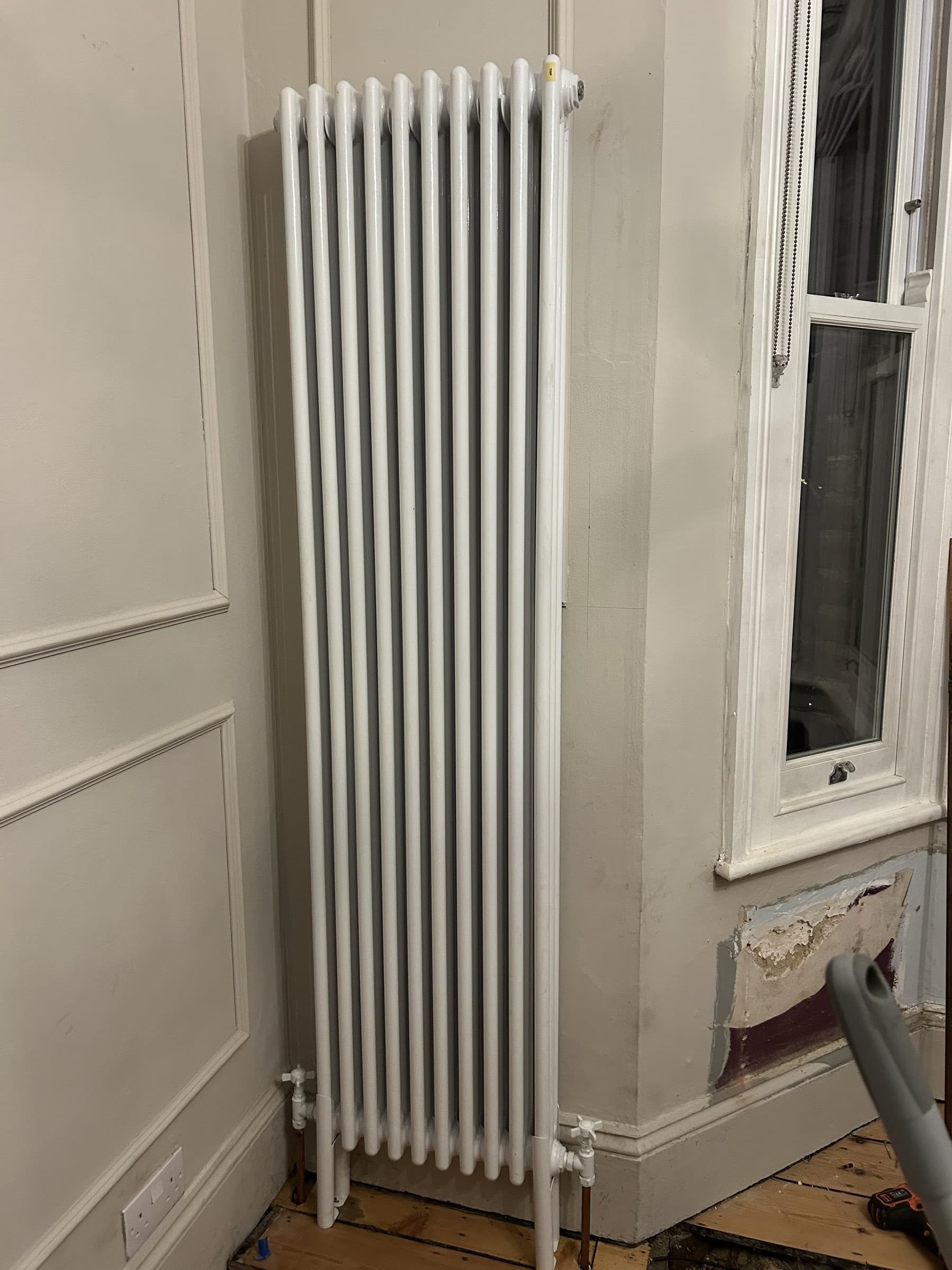 New tall white column radiator installed under a sash window with valve fittings connected