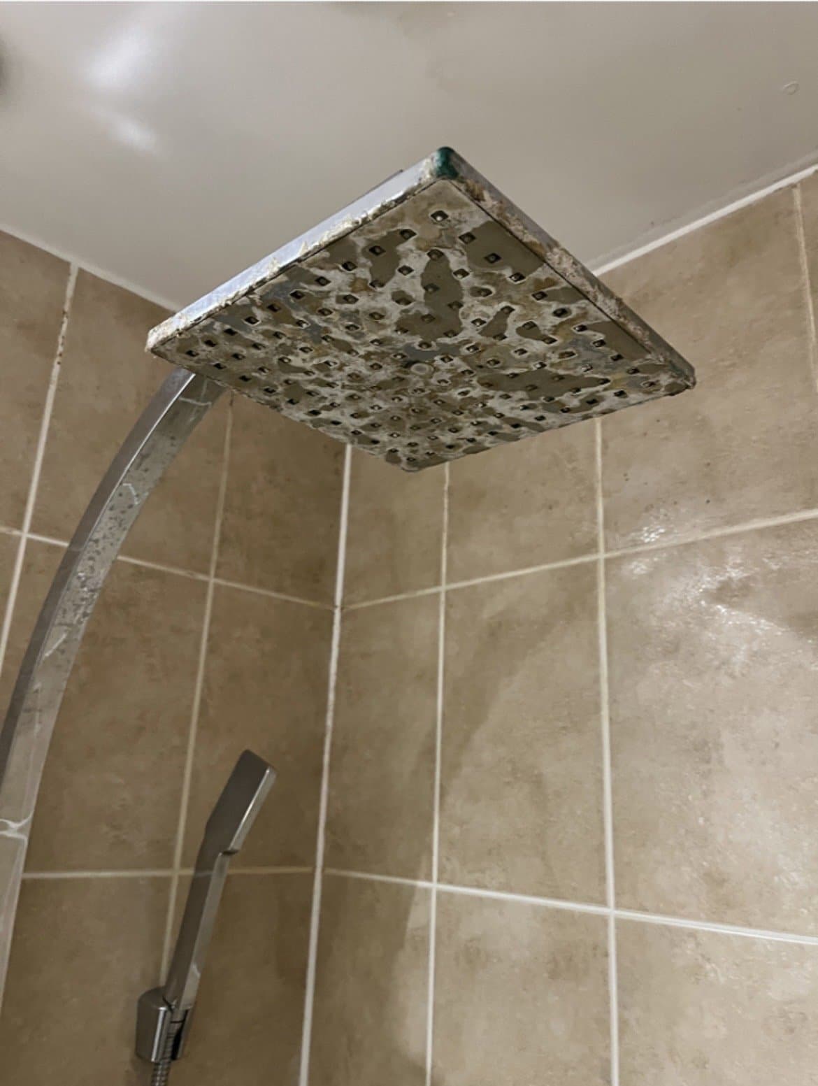 Old, heavily limescaled square shower head before replacement