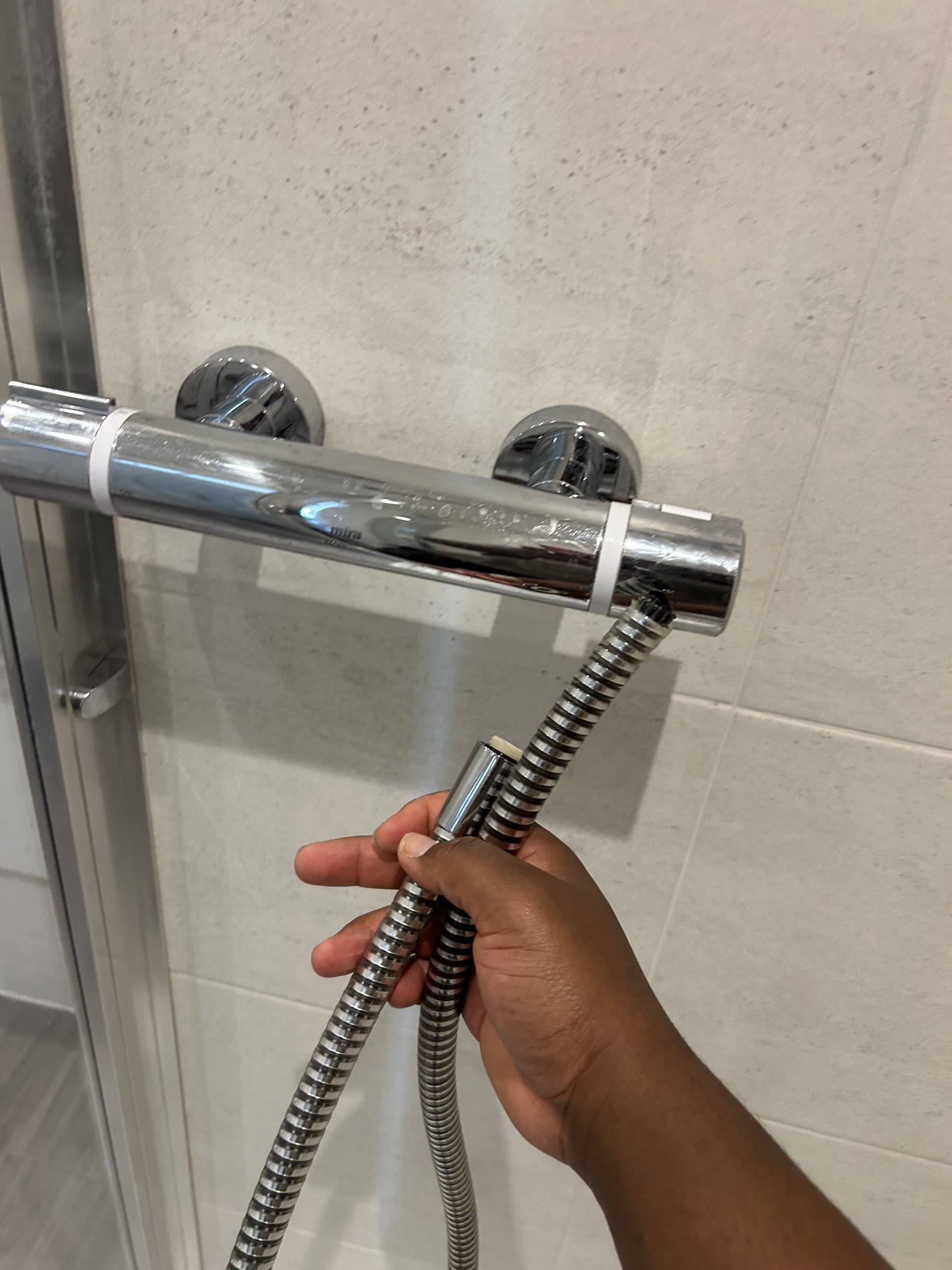 Old shower head and hose being detached from a wall-mounted shower slide rail