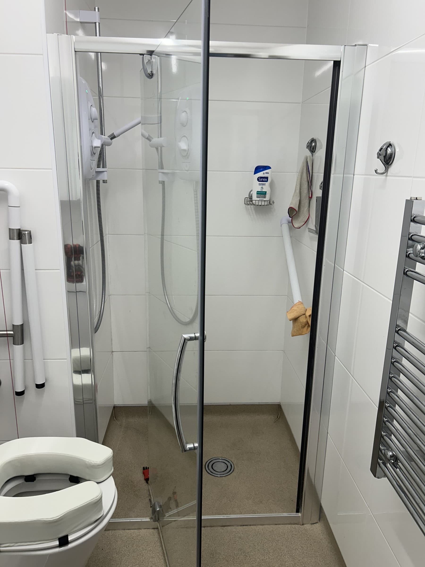Glass shower screen and electric shower installed in a fully tiled accessible bathroom with grab rails
