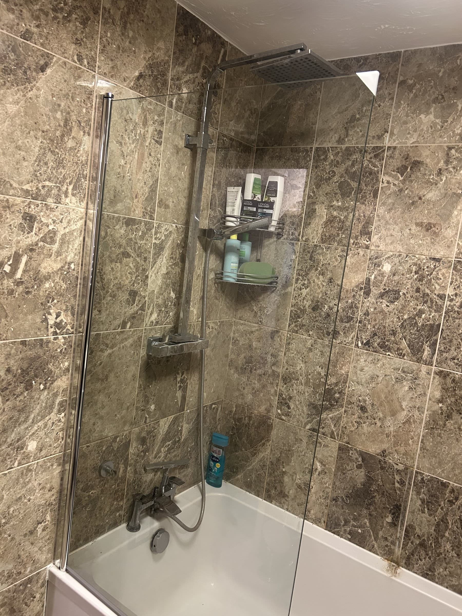 Glass shower screen installed over a bath with chrome fixing rail