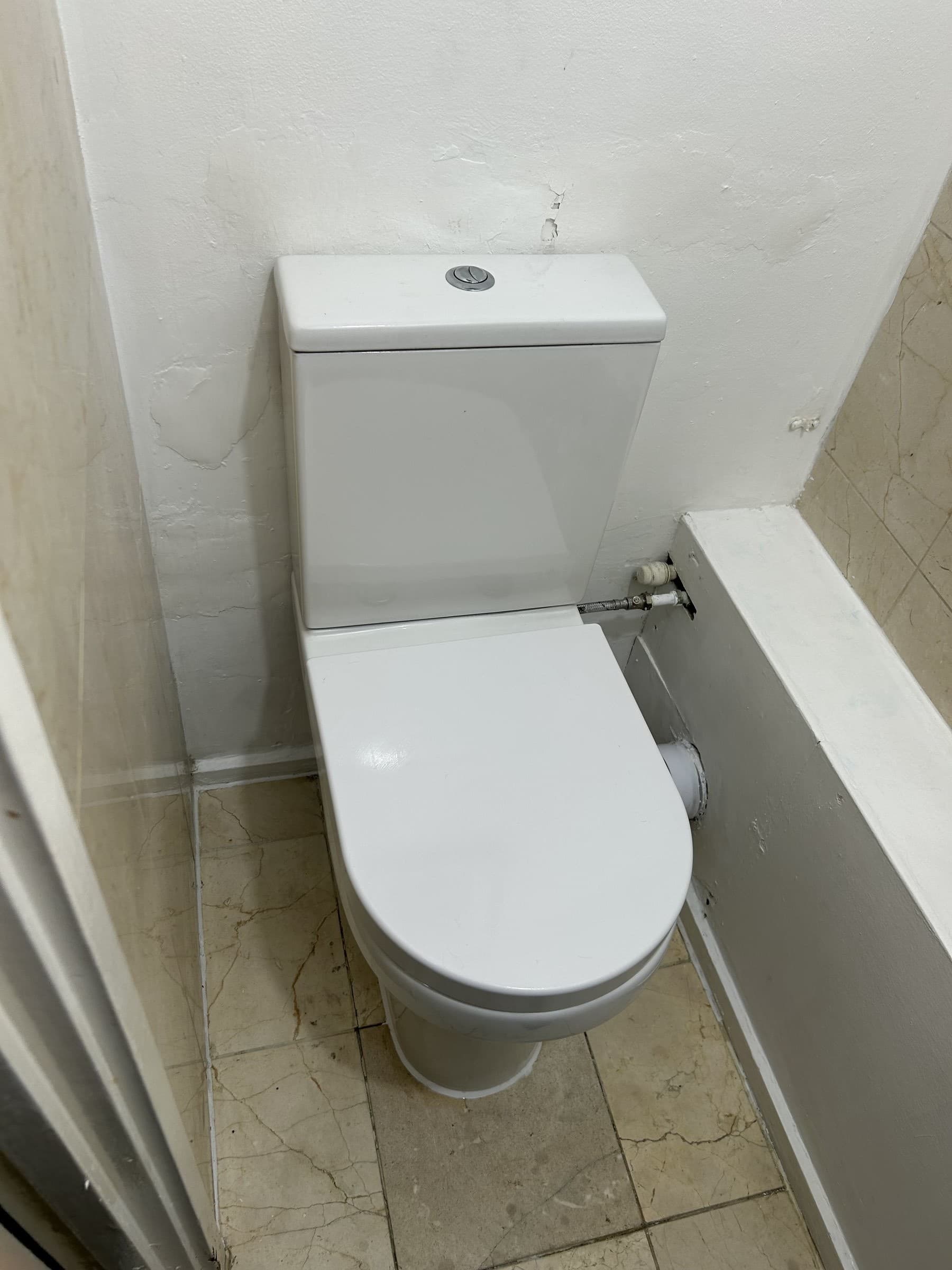 New wall-hung toilet with dual-flush cistern installed against a fully tiled wall