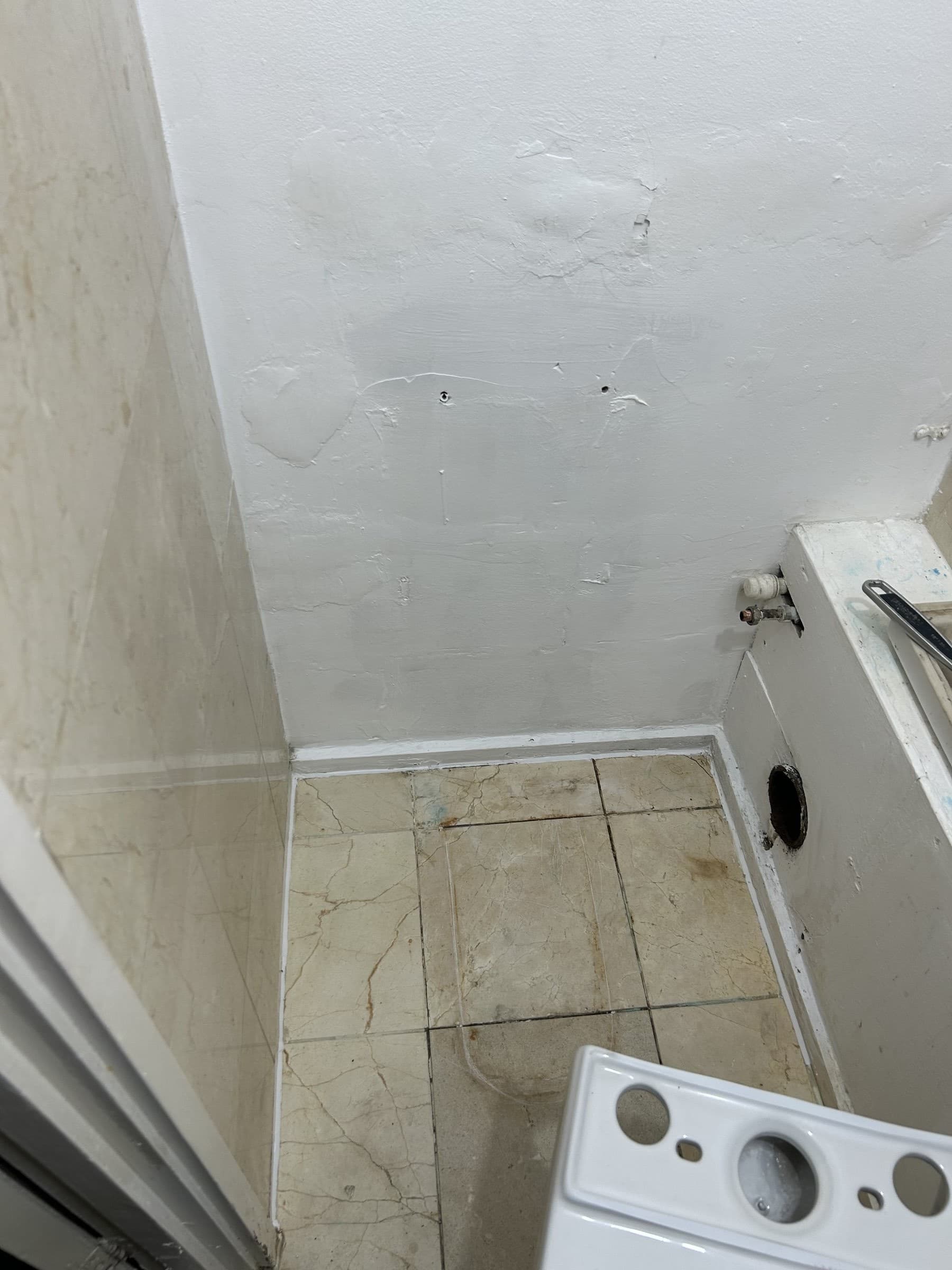 Bare plastered wall corner with capped pipework before a new toilet is installed